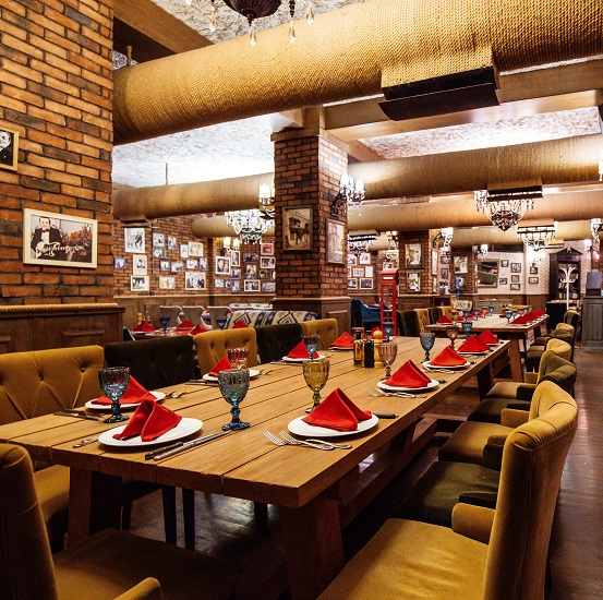 a restaurant hall with red brick walls wooden tables and pipes in the ceiling